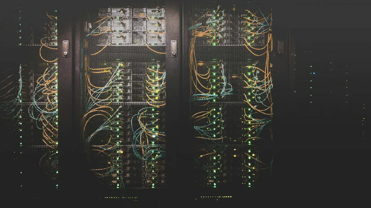 Serverschränke in einem abgedunkelten Rechenzentrum, dicht verlegte orange und türkise Patchkabel zwischen grün leuchtenden Statusanzeigen