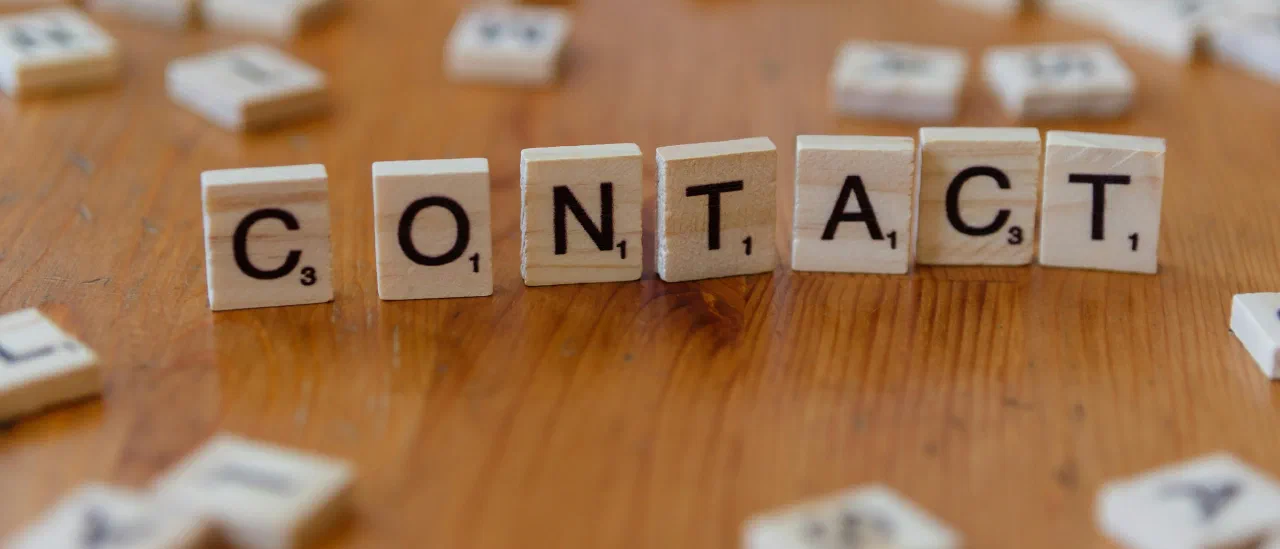 Scrabble-Steine auf einer Holzfläche, die das Wort CONTACT bilden